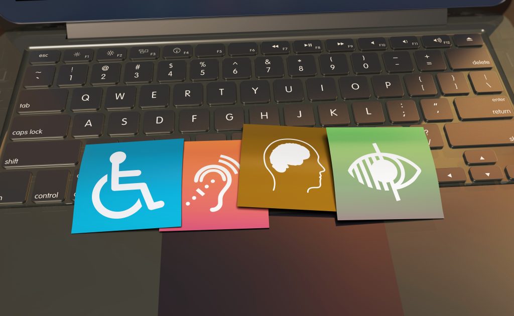 Four colorful squares with white accessibility icons (mobility, hearing, cognitive, and vision) placed on a laptop keyboard.