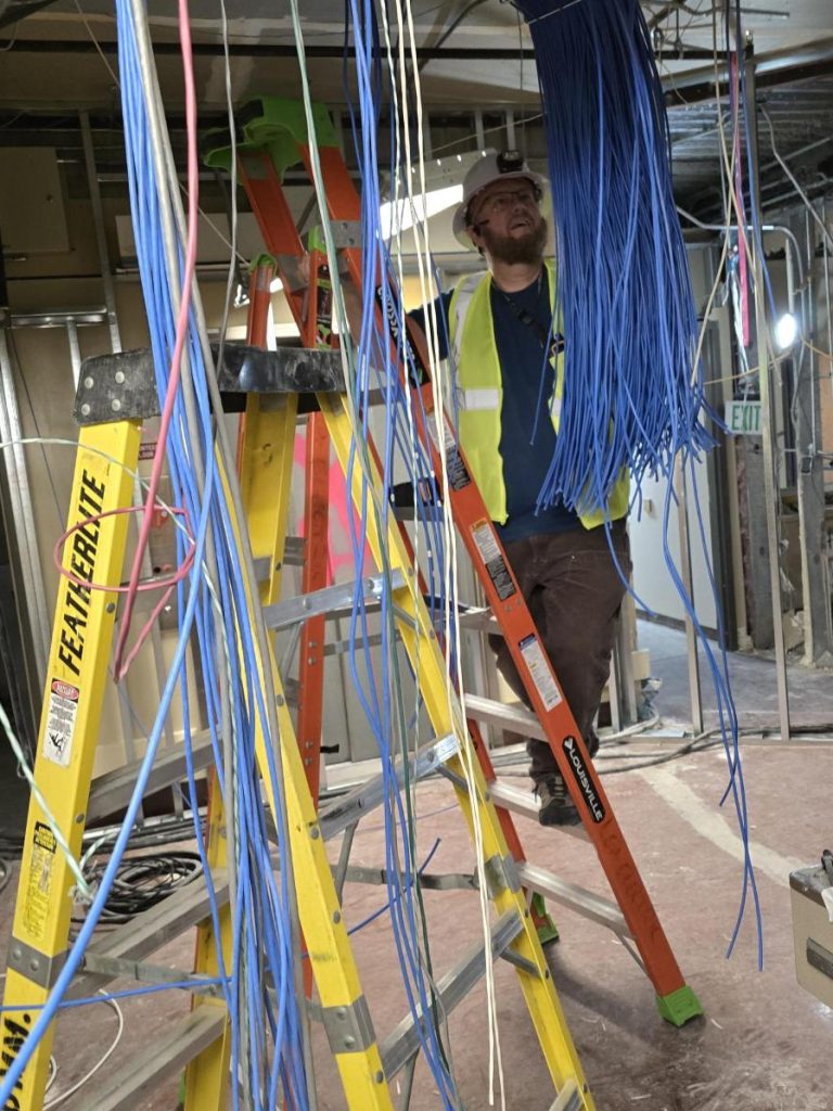 ITS employee working on fixing wires while standing on a ladder.