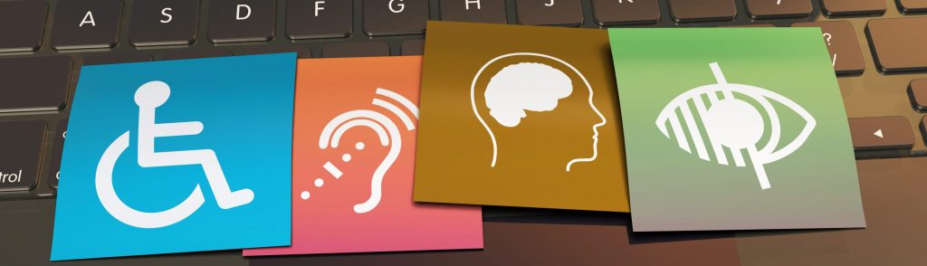 Four accessibility icons—a wheelchair symbol, an ear with sound waves, a head profile, and an eye symbol—displayed on colorful cards placed on a laptop keyboard.
